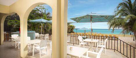 Une terrasse extérieure avec des tables et des chaises blanches, une piscine et une vue sur la plage.