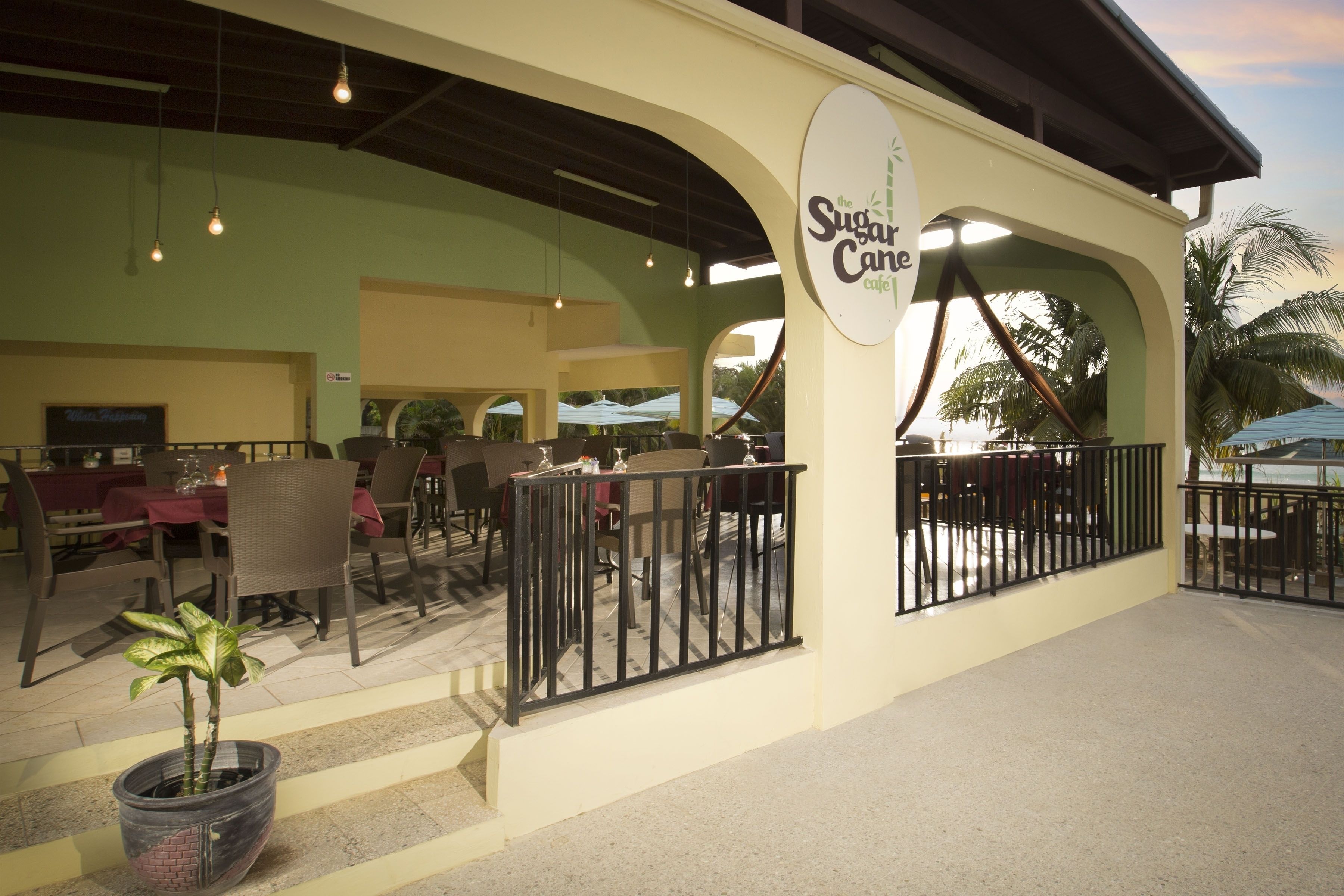 Un espace extérieur aménagé avec des tables et des chaises, un pot de fleurs et un panneau sur le mur, devant le Sugar Cane Cafe.