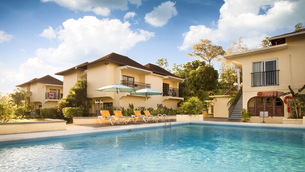 A swimming pool with lounge chairs and umbrellas, surrounded by buildings with balconies and a clear sky. - Rooms on the Beach Negril (Negril)
