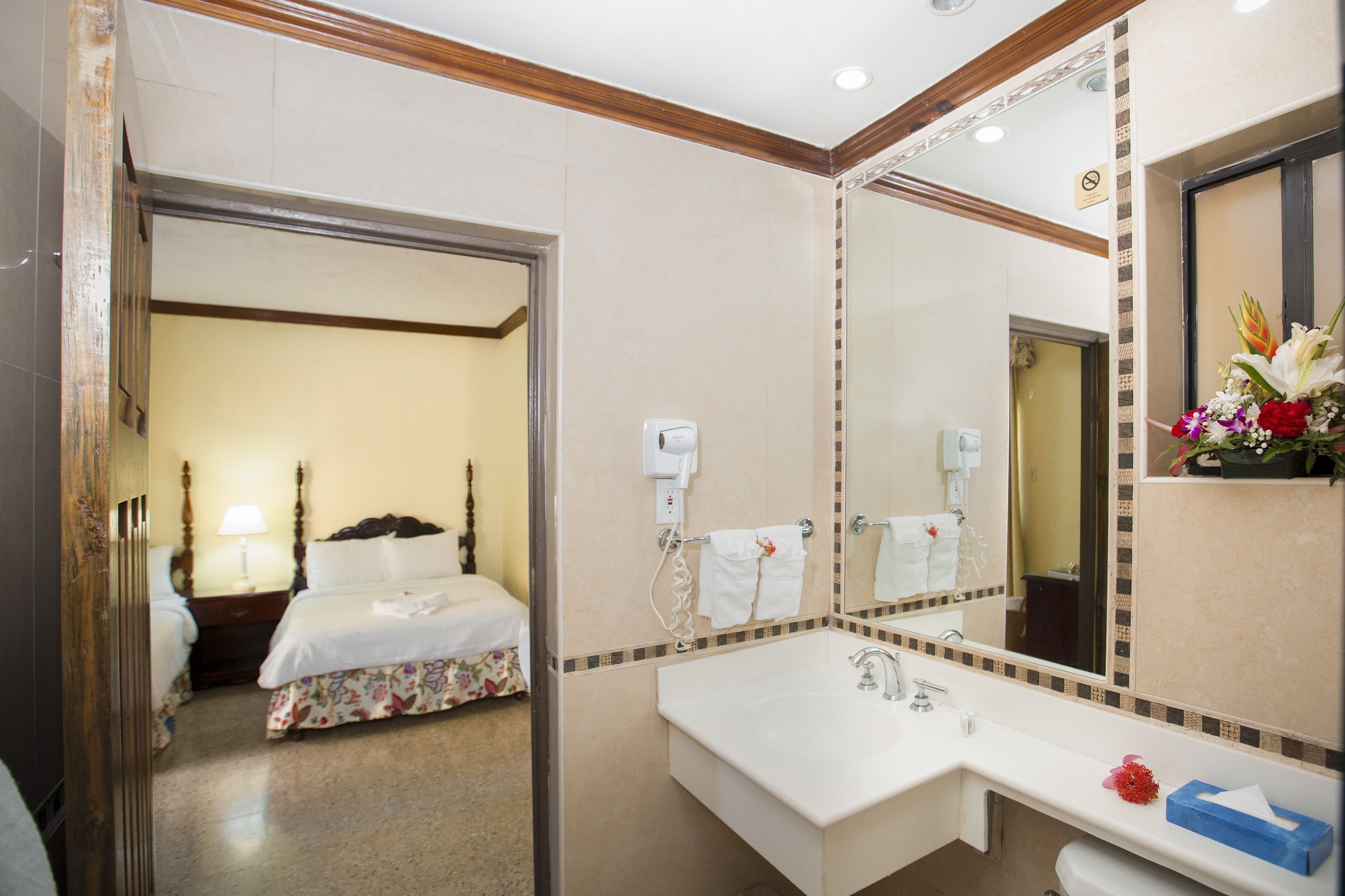 Hotelkamer met een bed, een badkamer met wastafel, spiegel en een bloemenarrangement.