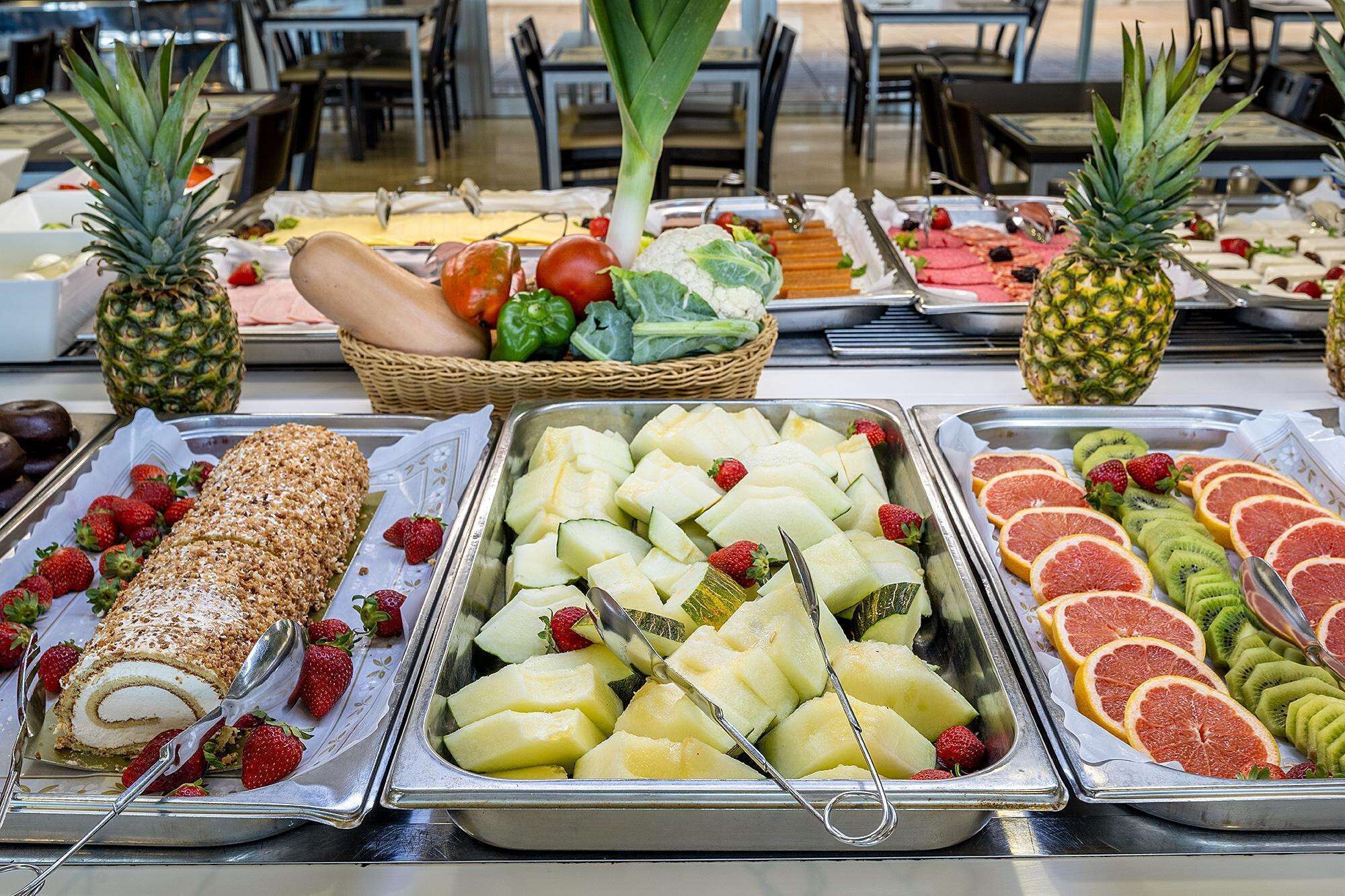 Un bufé con diversos alimentos, incluyendo un postre enrollado, fruta y verduras.