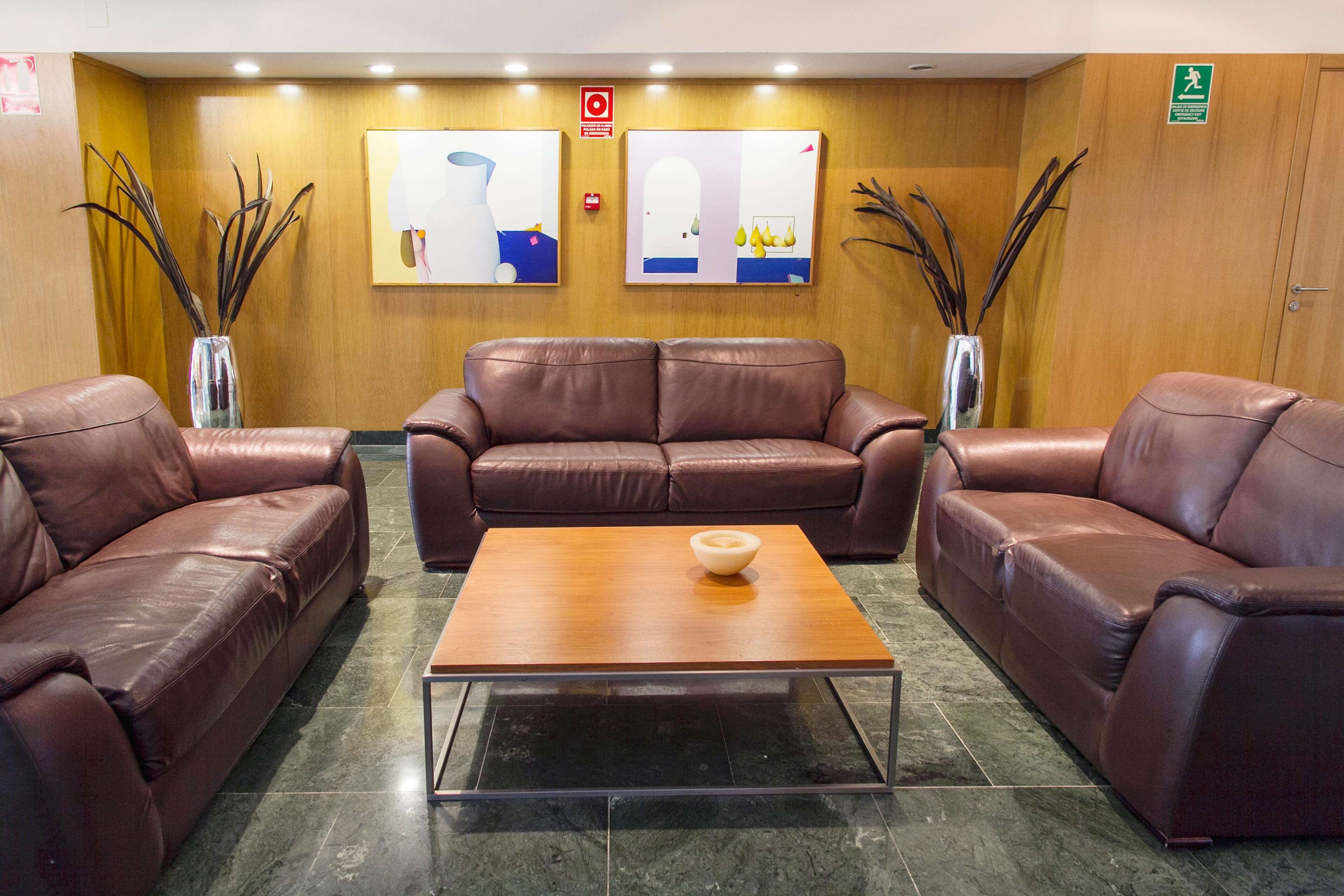 A lobby with leather sofas, a wooden coffee table, and two wall-mounted paintings.