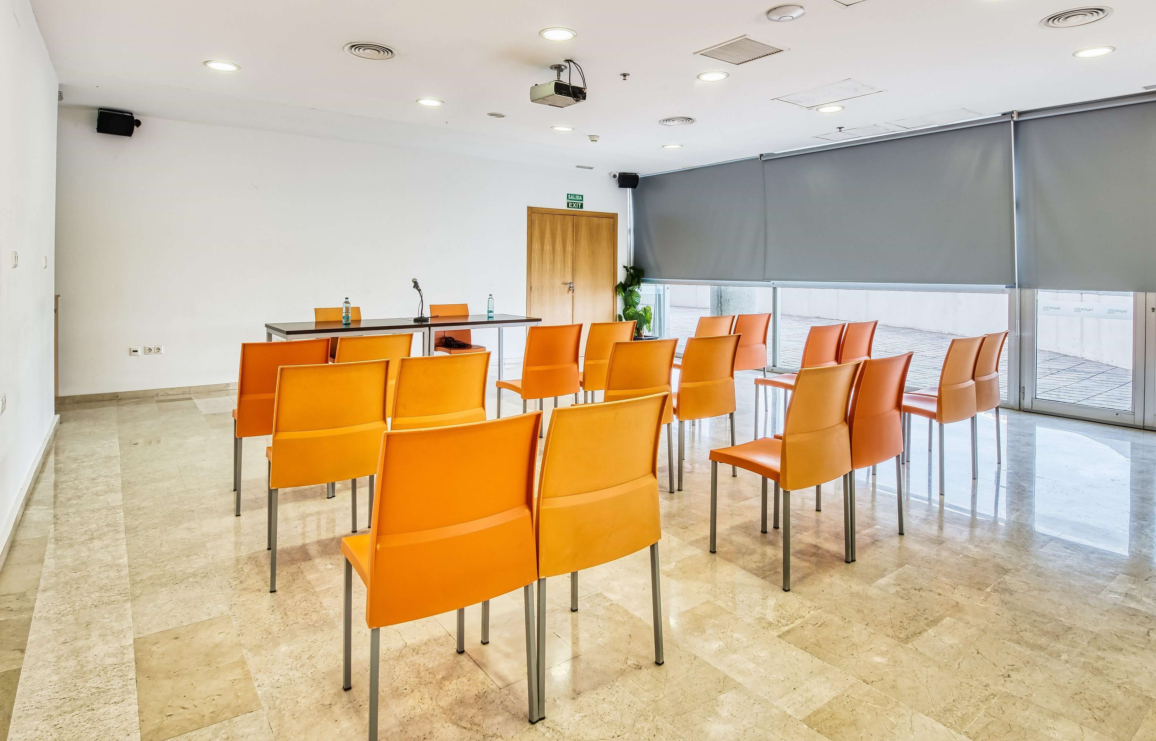 Un salón de conferencias con una mesa, sillas, un proyector y un amplio ventanal.