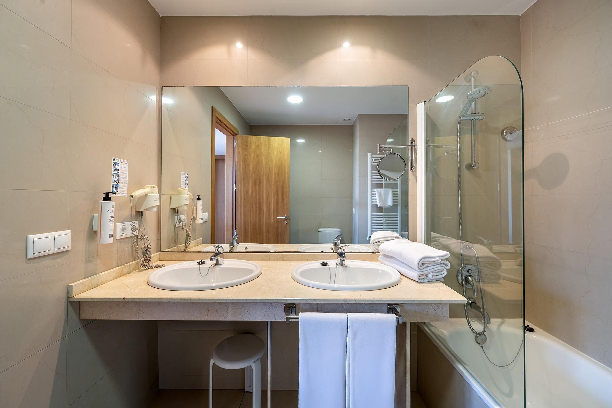 Un baño moderno con dos lavamanos, cabina de ducha con mampara de vidrio y un espejo sobre el lavamanos.