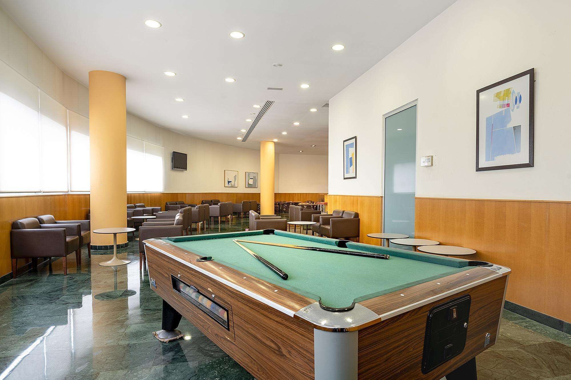 A pool table in a room with multiple seating areas and a large window.
