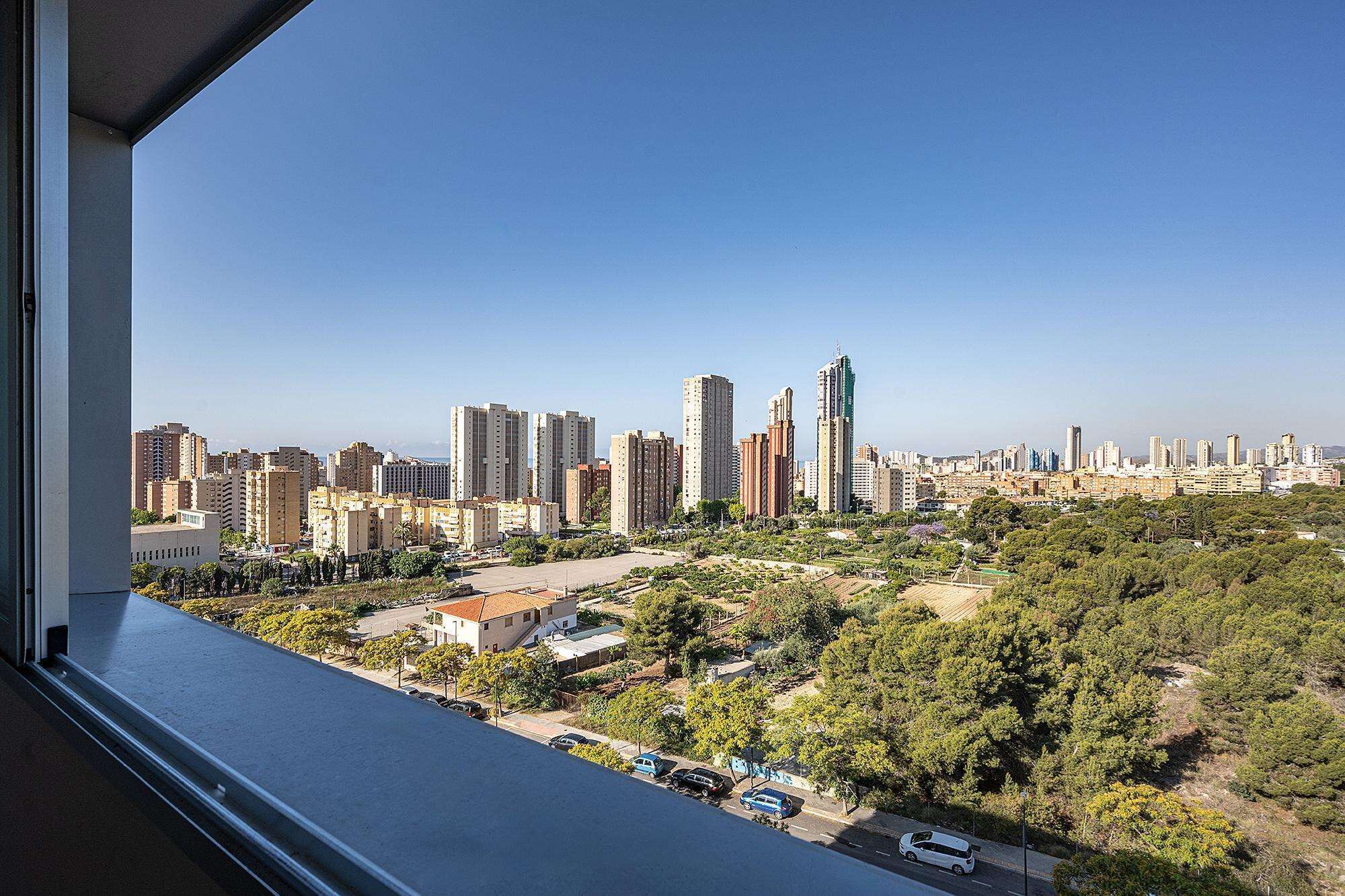 A cityscape with high-rise buildings and a view of a residential area with trees and parked cars.