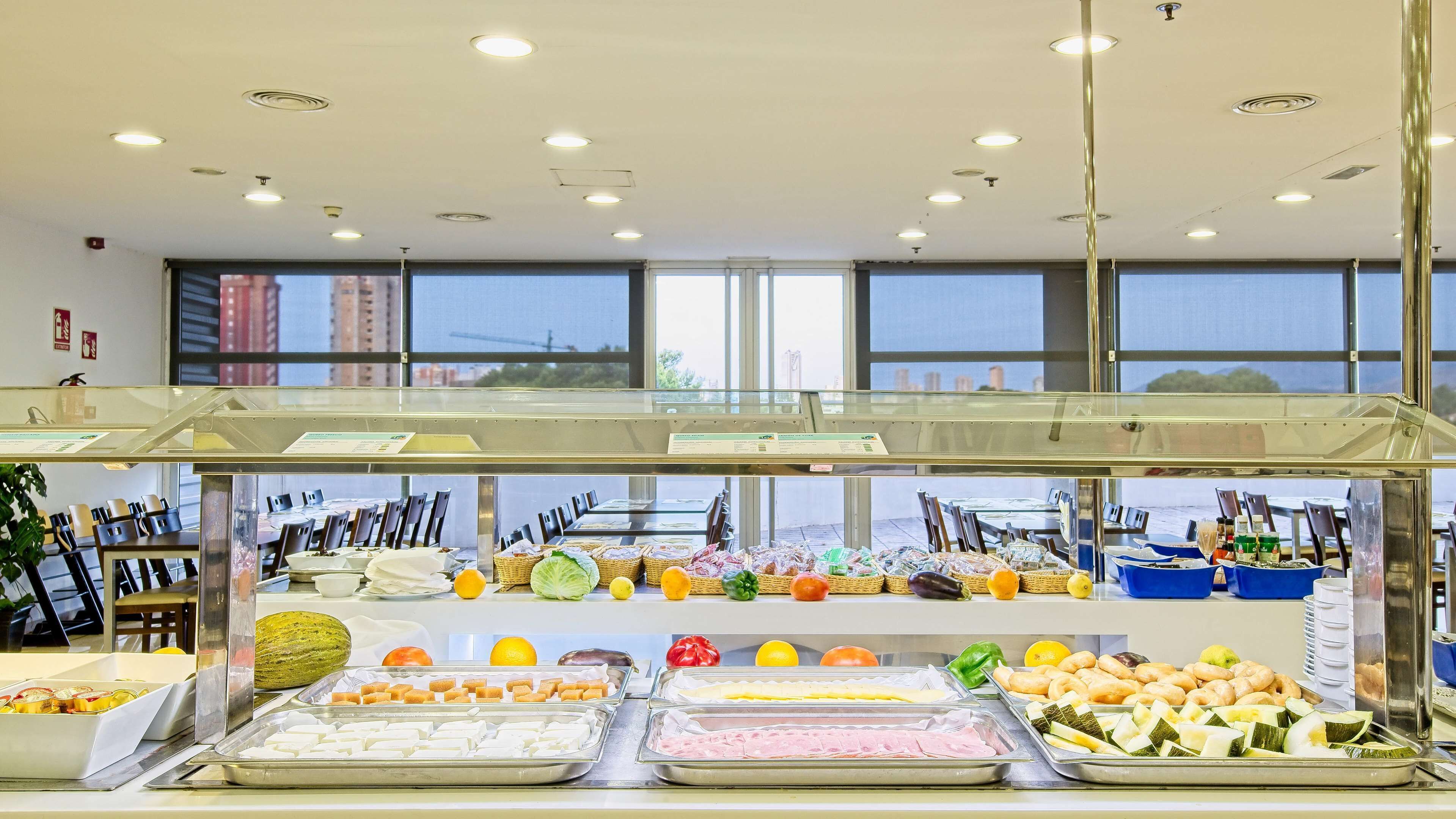A buffet with various food items and a view of the city through large windows.