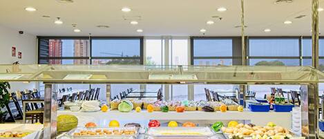 A buffet with various food items and a view of the city through large windows.