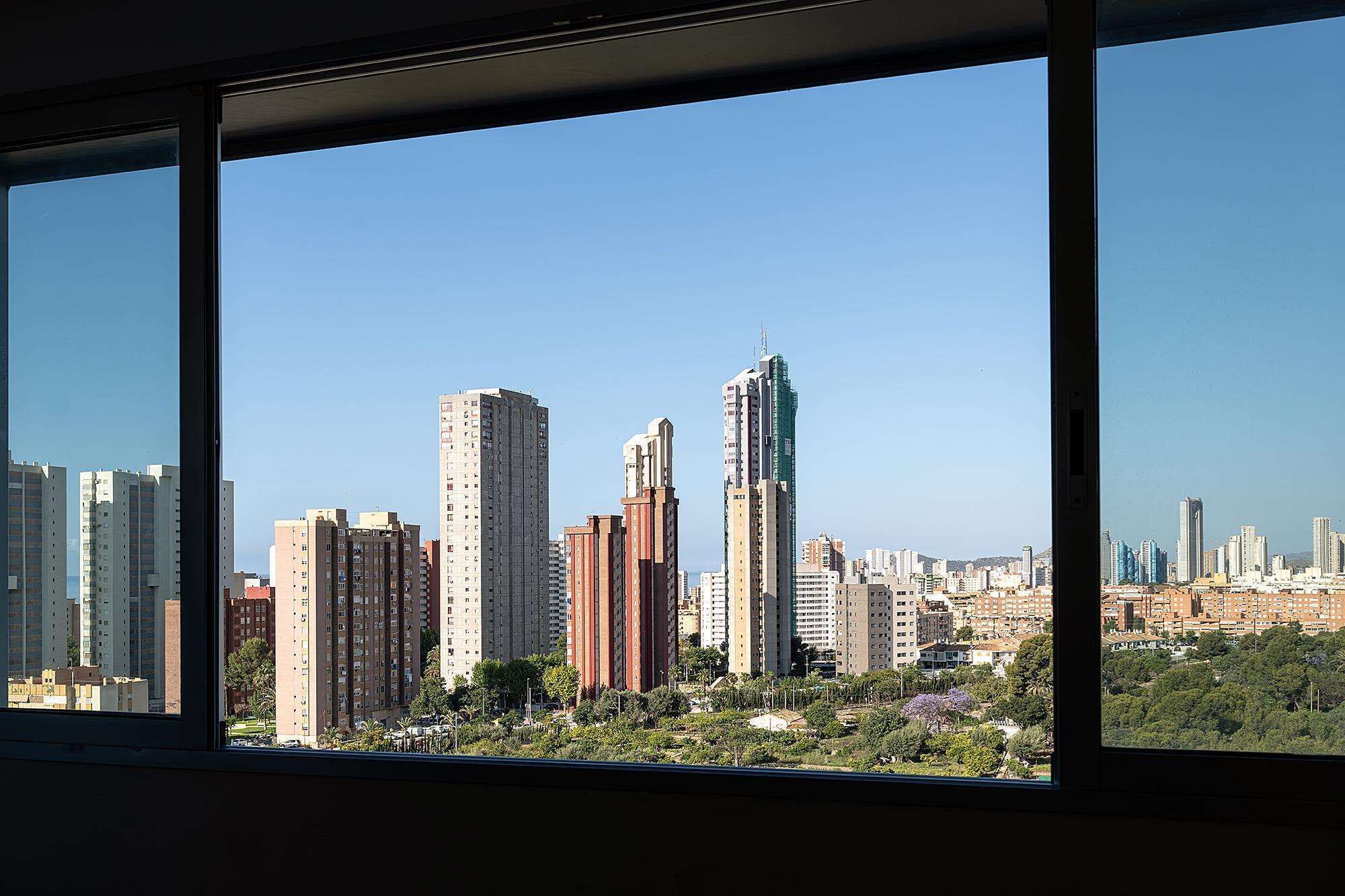Un paisaje urbano con rascacielos, incluyendo un distintivo rascacielos verde, visto a través de una ventana.