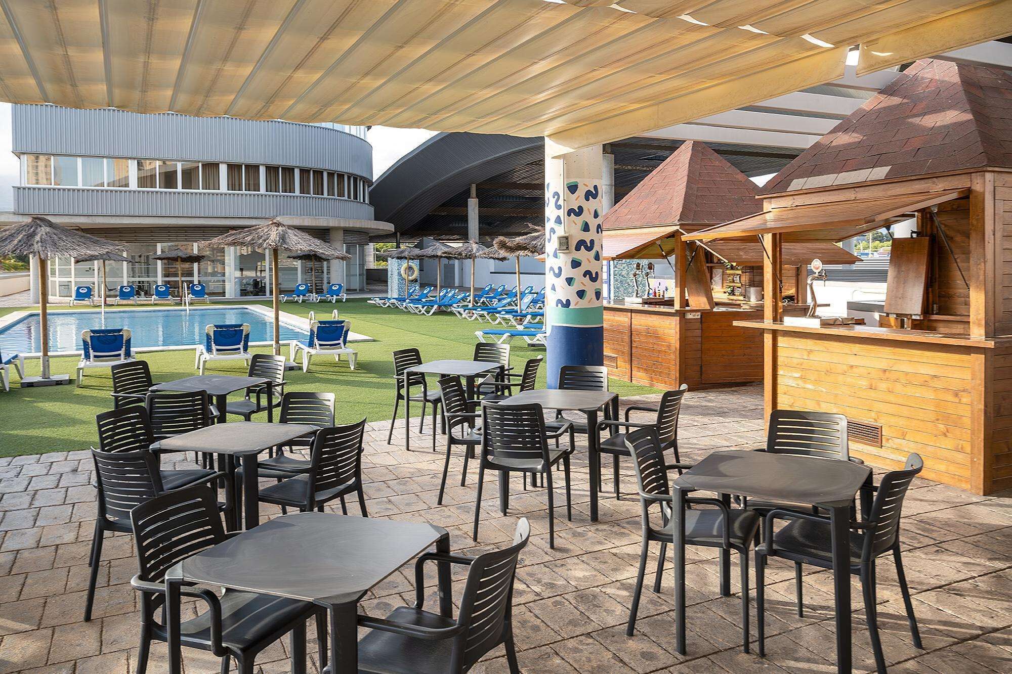 An outdoor patio area with tables and chairs, a pool, and a bar area.
