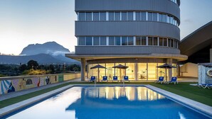 Un edificio moderno con piscina y sillones de descanso.