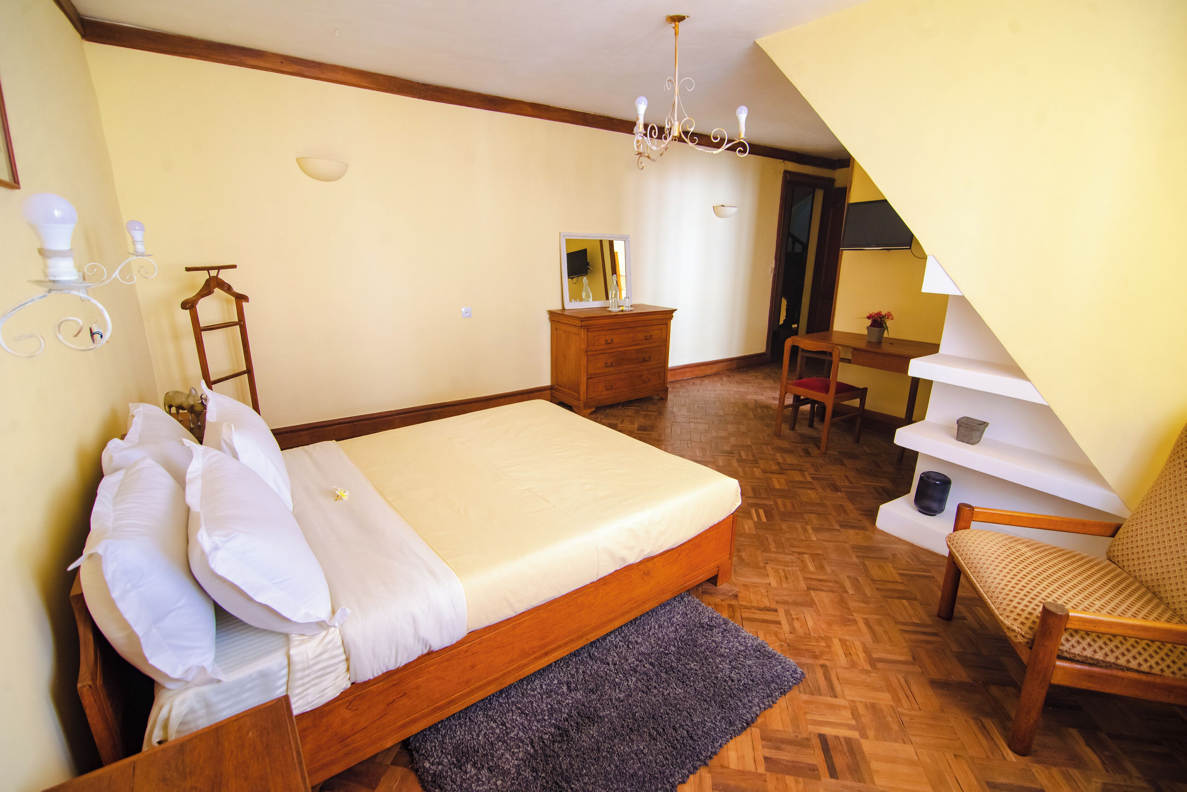 Un dormitorio con una cama de madera, un aparador, una silla, un escritorio y una escalera.