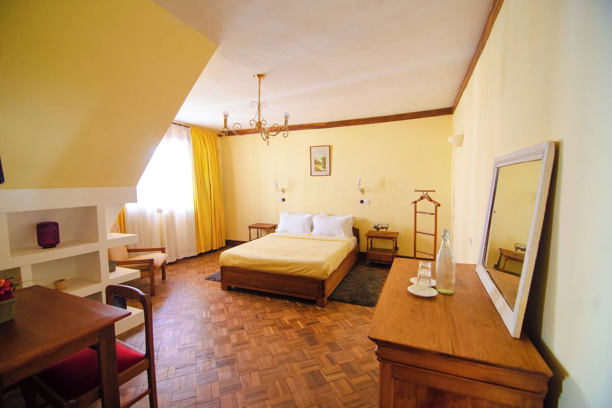 A bedroom with a wooden bed, bedside tables, a dresser, a chair, and a mirror.