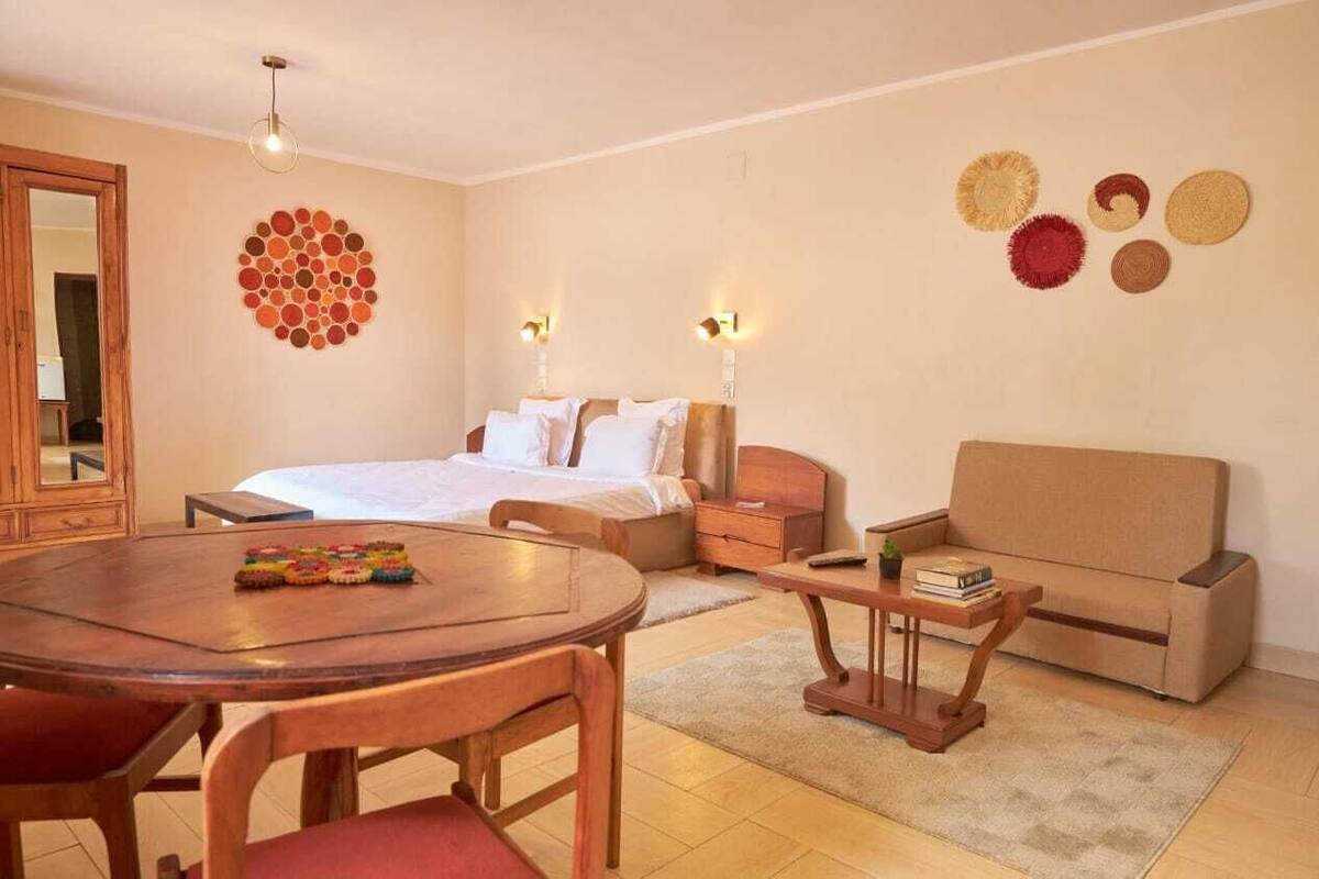 A hotel room with a bed, a wooden table, a sofa, and a mirror.