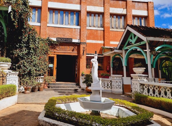 Un área de recepción con un letrero, una estatua y un edificio de ladrillo con entrada de azulejos.