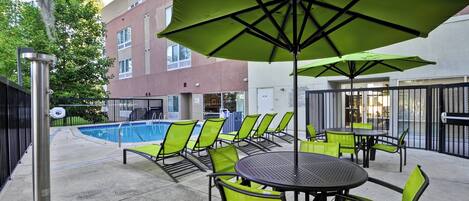 Zona de piscina con sillas y sombrillas verdes, una piscina y un edificio con un letrero que dice 'SpongHill Suites'.