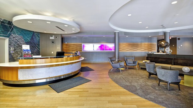 A modern reception area with a curved desk, seating, and a large digital display. - SpringHill Suites Tallahassee Central (Tallahassee)