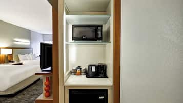 A hotel room with a bed, a television, a microwave, a coffee maker, and a refrigerator.