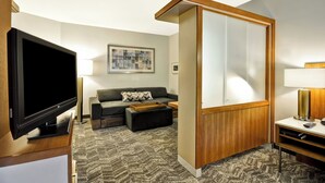 A modern hotel room with a flat-screen TV, a sofa, a coffee table, and a wooden partition. - SpringHill Suites Tallahassee Central (Tallahassee)