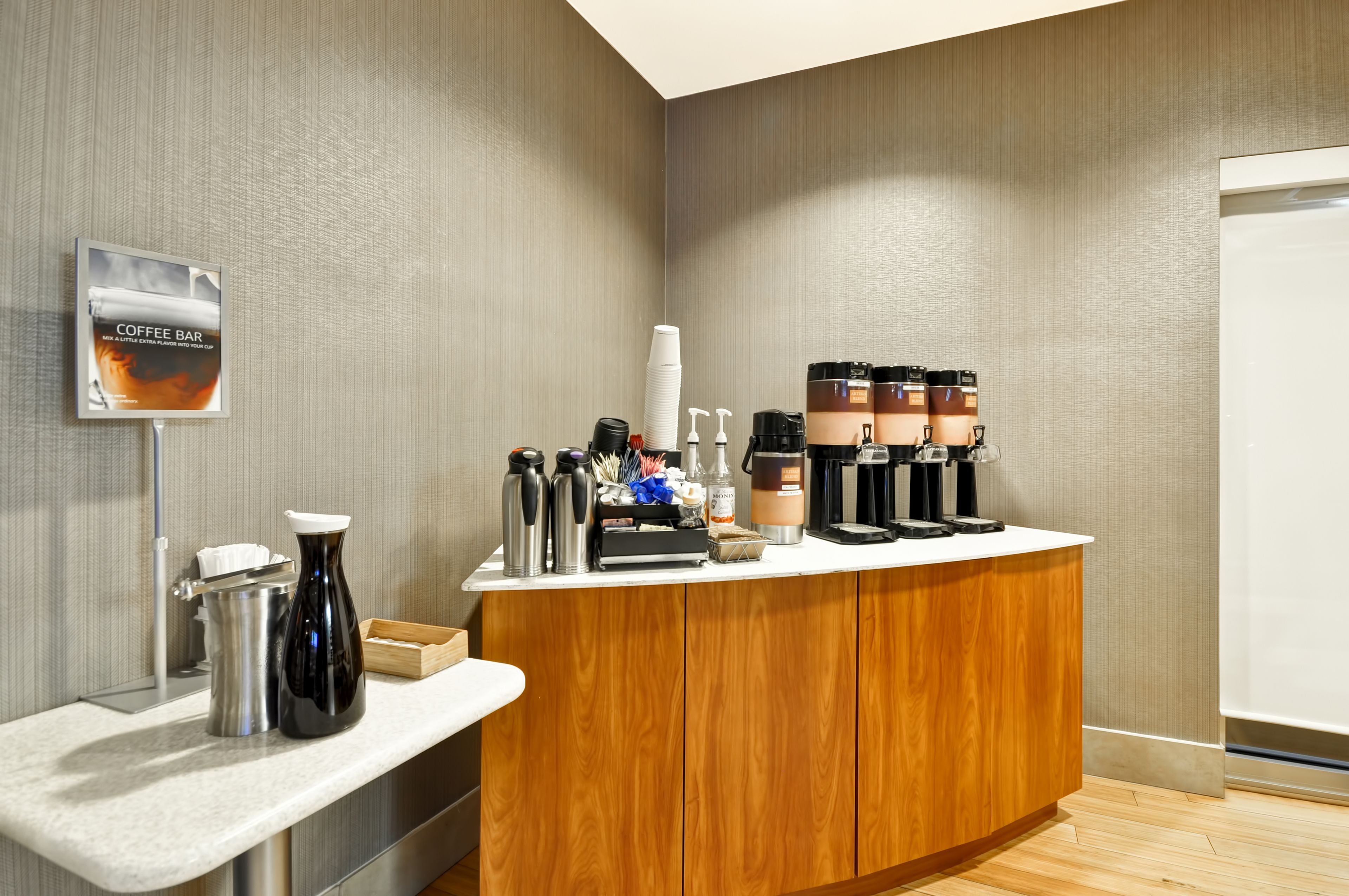 A coffee bar with a sign, coffee makers, and various coffee cups.