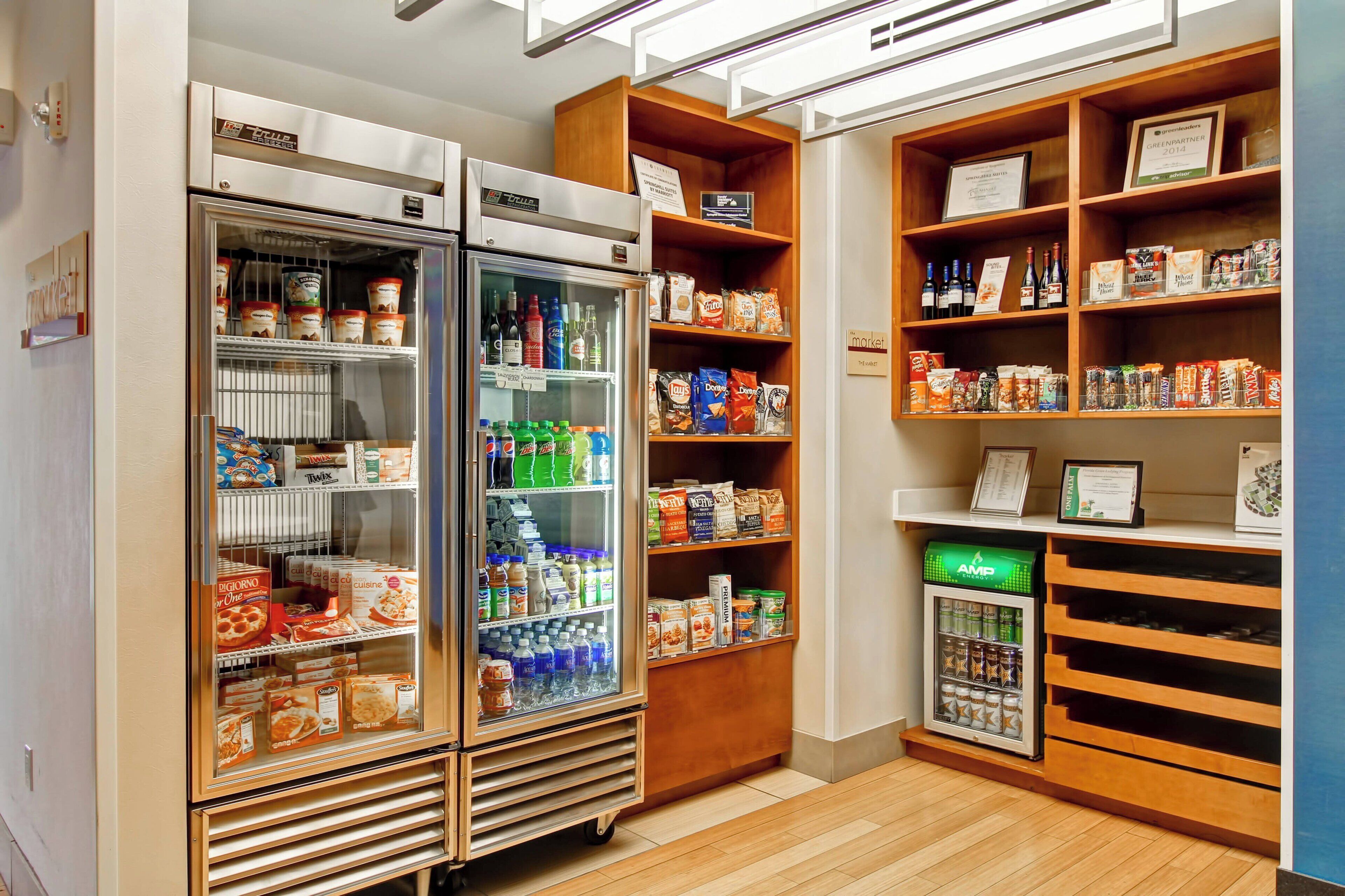 A well-organized room with two large refrigerators stocked with beverages and snacks, wooden shelves with various food items, and a small vending machine.