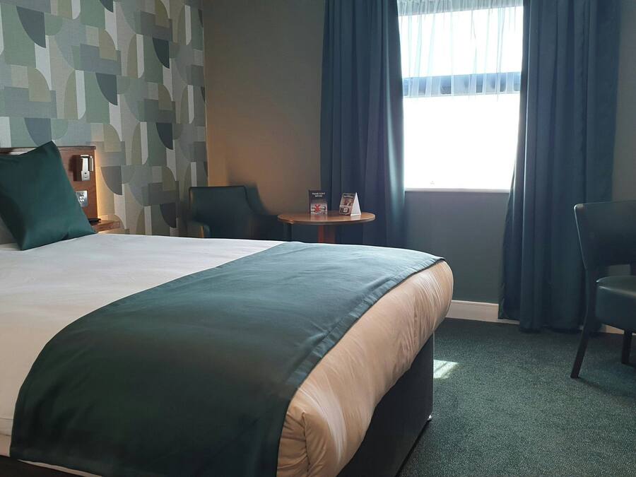 A hotel room with a large bed, a desk, a chair, a small table, and a window with curtains.