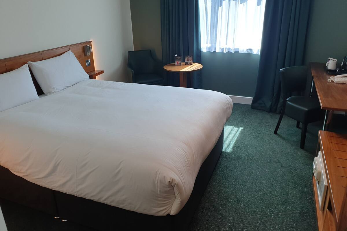 A hotel room with a large bed, a small round table, a chair, and a desk with a telephone.