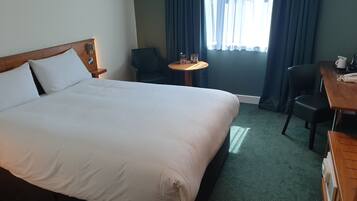 A hotel room with a large bed, a small round table, a chair, and a desk with a telephone.