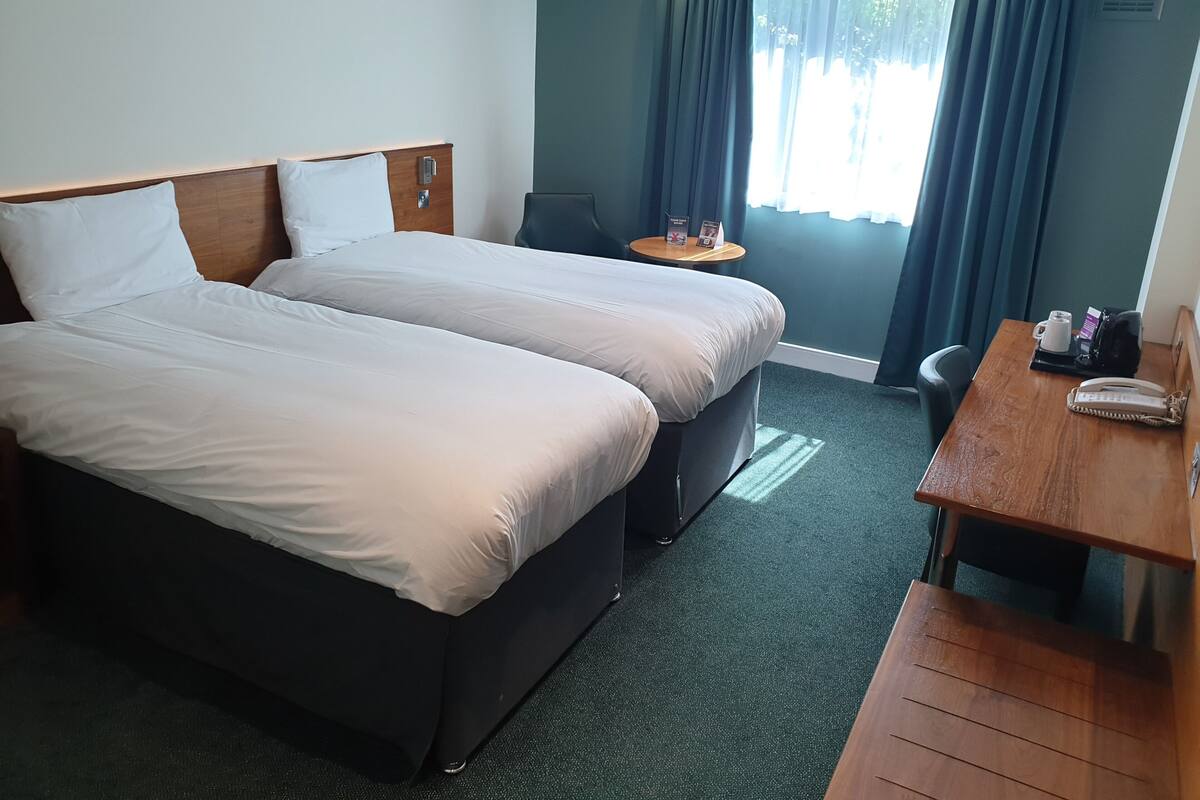 A hotel room with two beds, a small table, a chair, and a desk with a telephone.