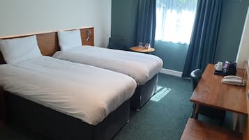 Habitación de hotel con dos camas, una mesita, una silla y un escritorio con teléfono.