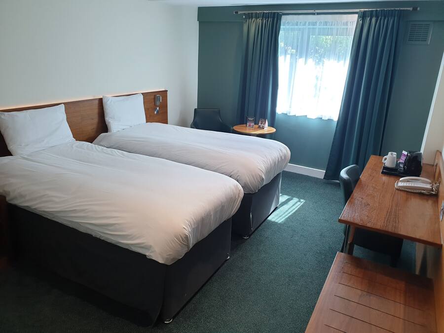 Habitación de hotel con dos camas, una mesita, una silla y un escritorio con teléfono.