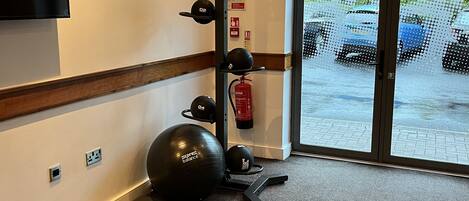 A fitness area with exercise equipment, a flat-screen TV, and a view of parked cars outside.