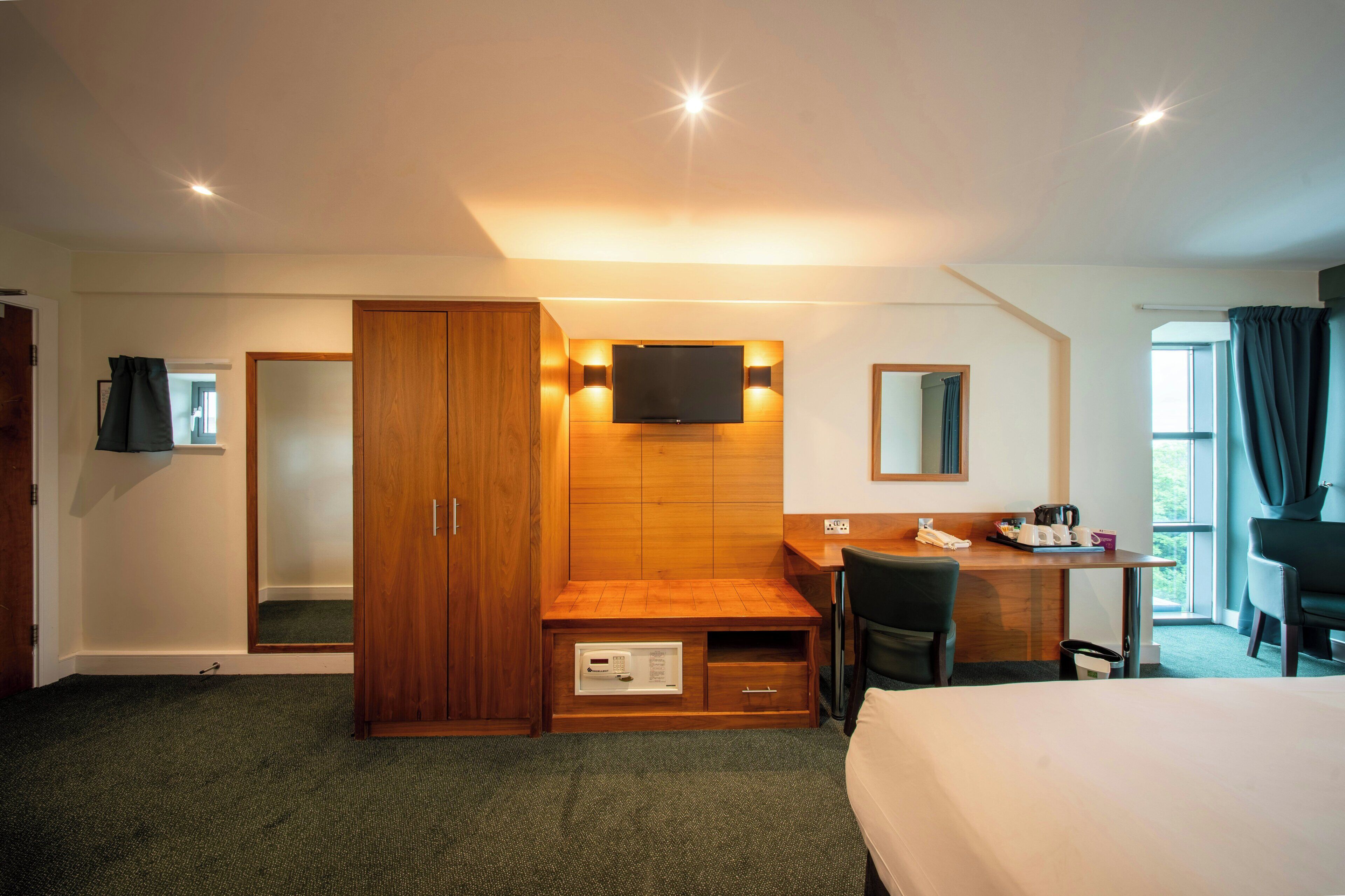 A hotel room with a bed, desk, chair, wardrobe, TV, and a window with curtains.
