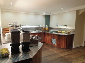 A modern kitchen with a breakfast bar, coffee machines, and a fruit display.