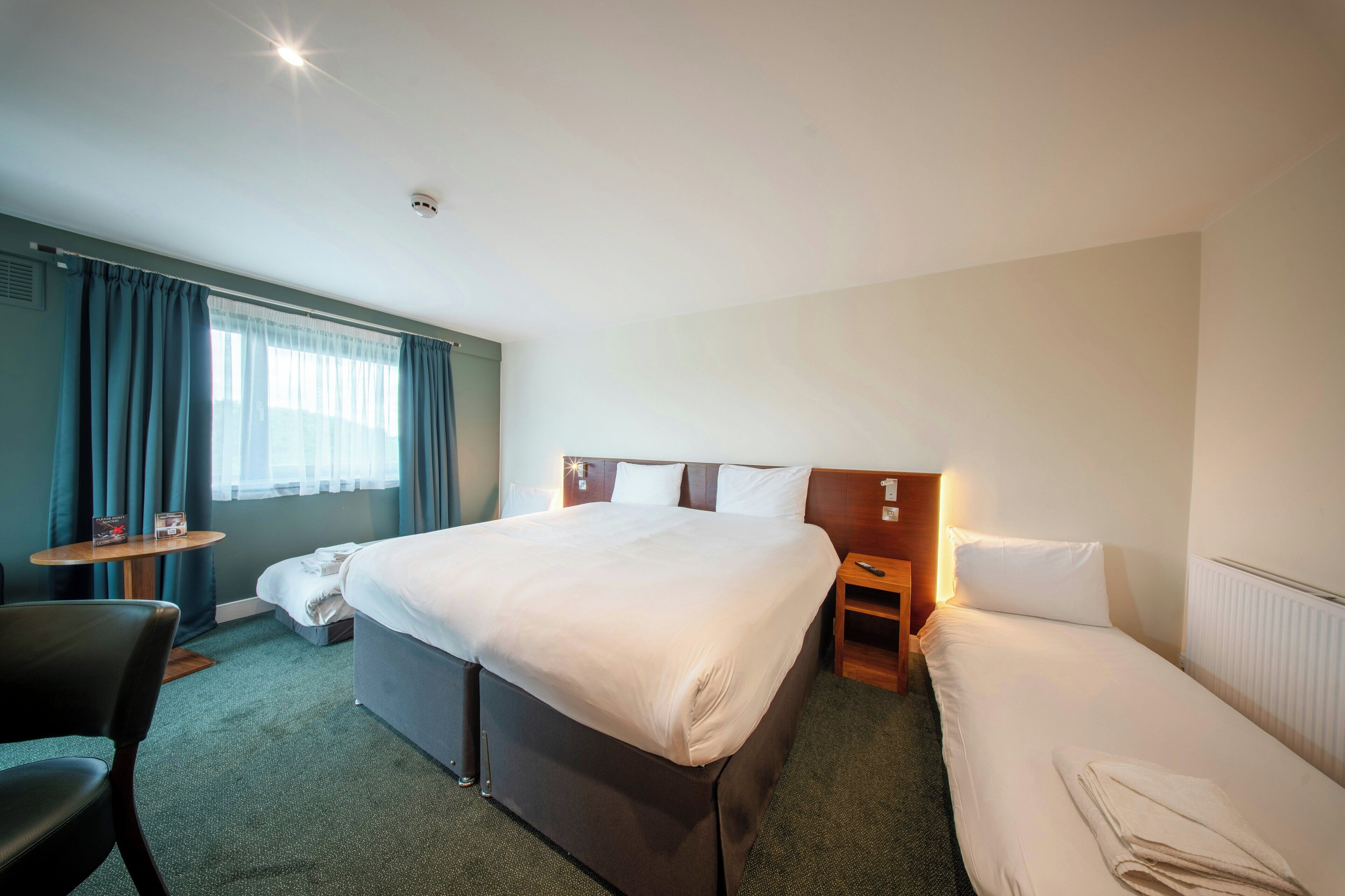 A hotel room with a large bed, a desk, a chair, and a window with curtains.