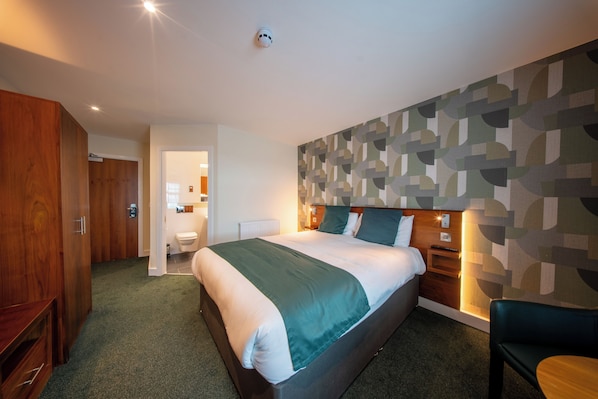 Habitación de hotel con una cama grande, un armario de madera, un baño y un papel tapiz estampado.