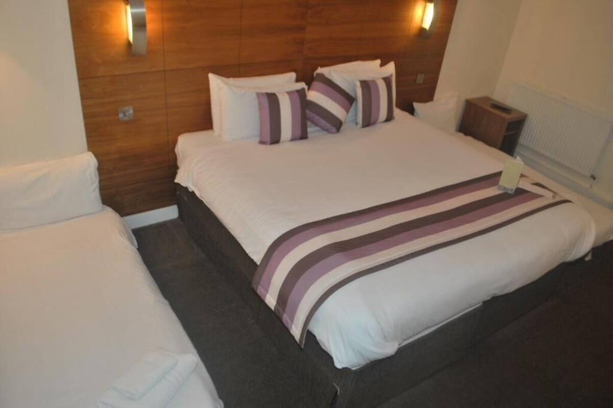 A hotel room with a wooden headboard, a large bed with striped bedding, a bedside table, and a nightstand.