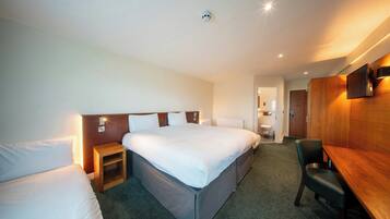 A hotel room with a large bed, a bedside table, a chair, a desk, and a bathroom visible through an open door.