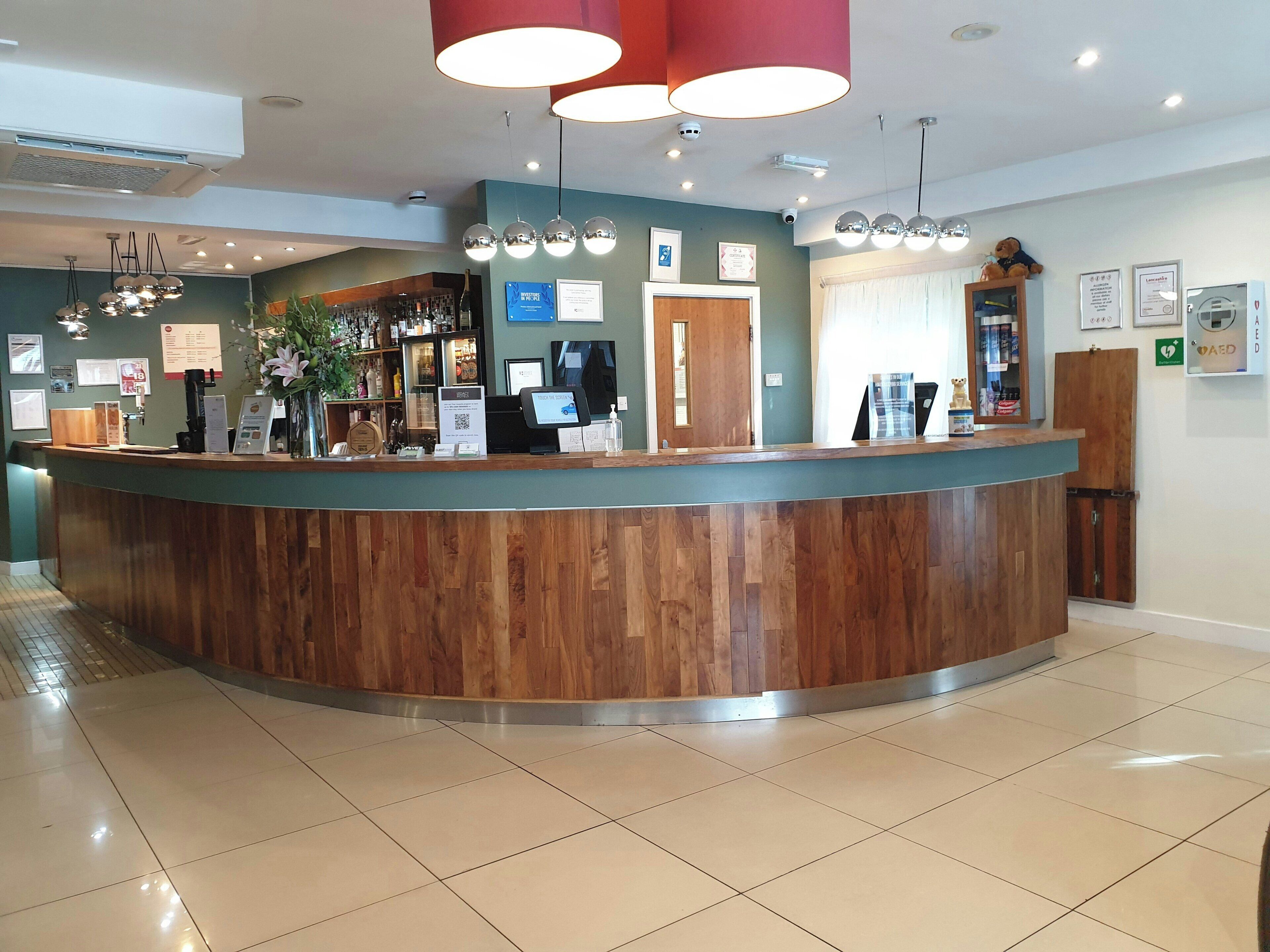 Zona de recepción con mostrador de madera, máquina de café y barra con varias botellas.