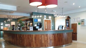 A reception area with a wooden counter, a coffee machine, and a bar with various bottles.