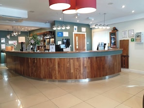 Zona de recepción con mostrador de madera, máquina de café y barra con varias botellas.