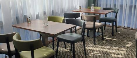 Habitación de hotel con comedor que incluye mesas y sillas, piso con diseño y cortinas de gasa.