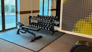 A gym with a bench, dumbbells, a treadmill, and a patterned wall. - Legacy Preston International Hotel (Preston)