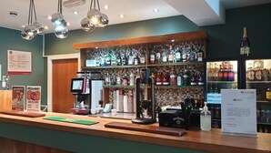 A bar area with a coffee machine, stacked glasses, and a variety of liquor bottles. - Legacy Preston International Hotel (Preston)