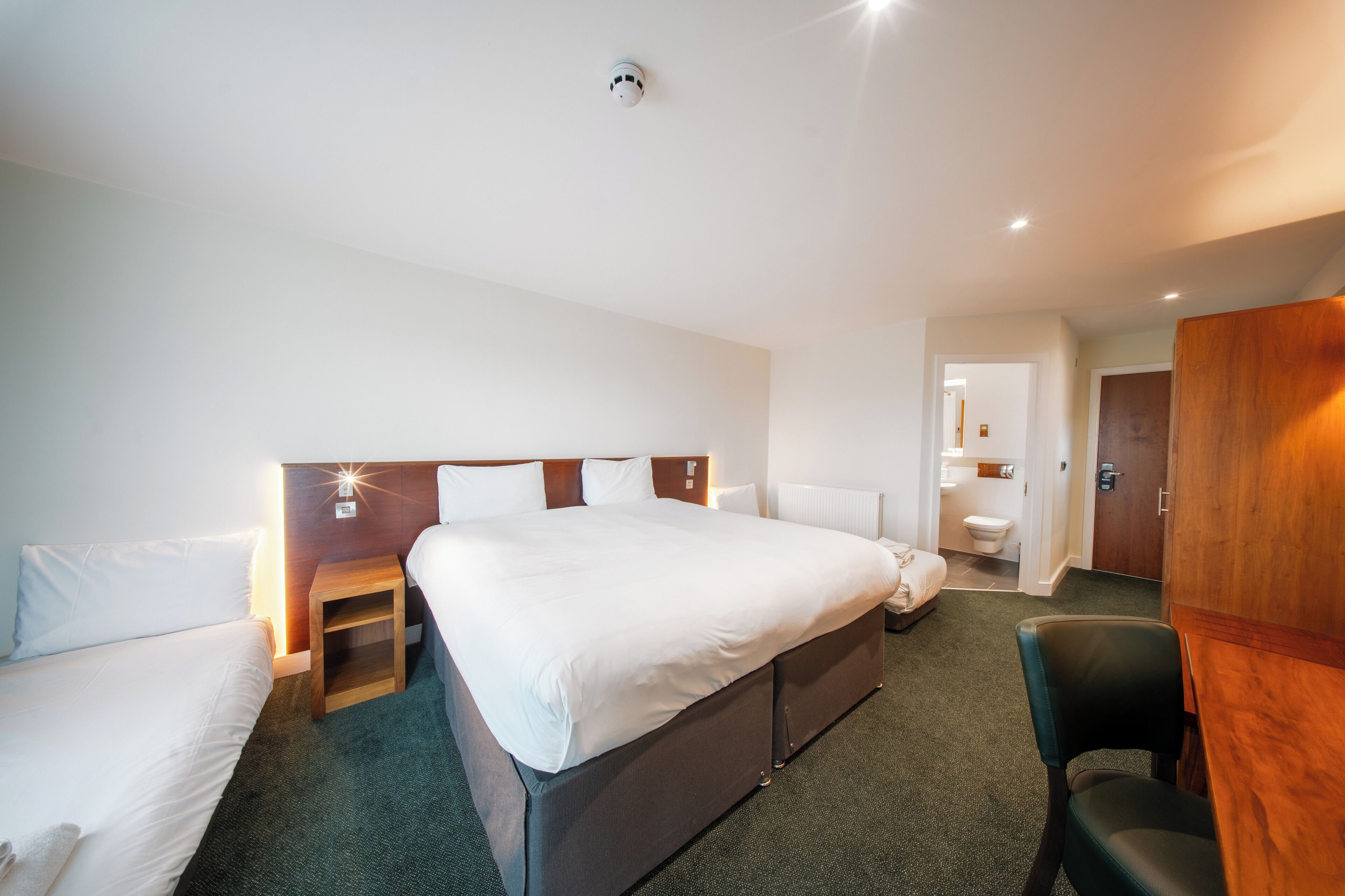 A hotel room with a large bed, two bedside tables, a chair, and a wooden wardrobe.