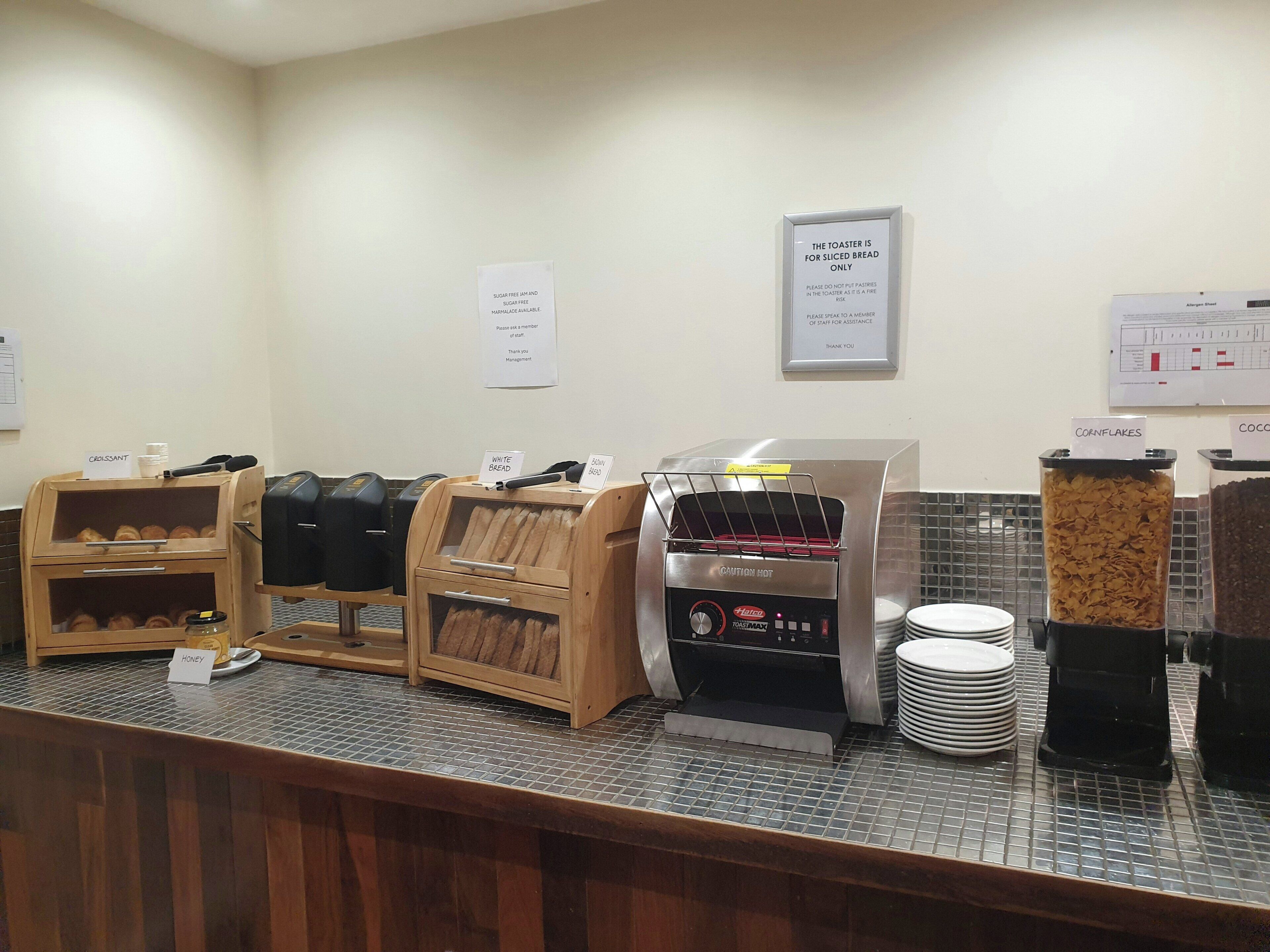 A self-service breakfast area with bread, pastries, and cereal options.