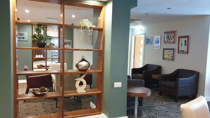 A hotel lobby with a patterned carpet, a wooden reception desk, a seating area with chairs, and a wall with framed artwork. - Legacy Preston International Hotel (Preston)