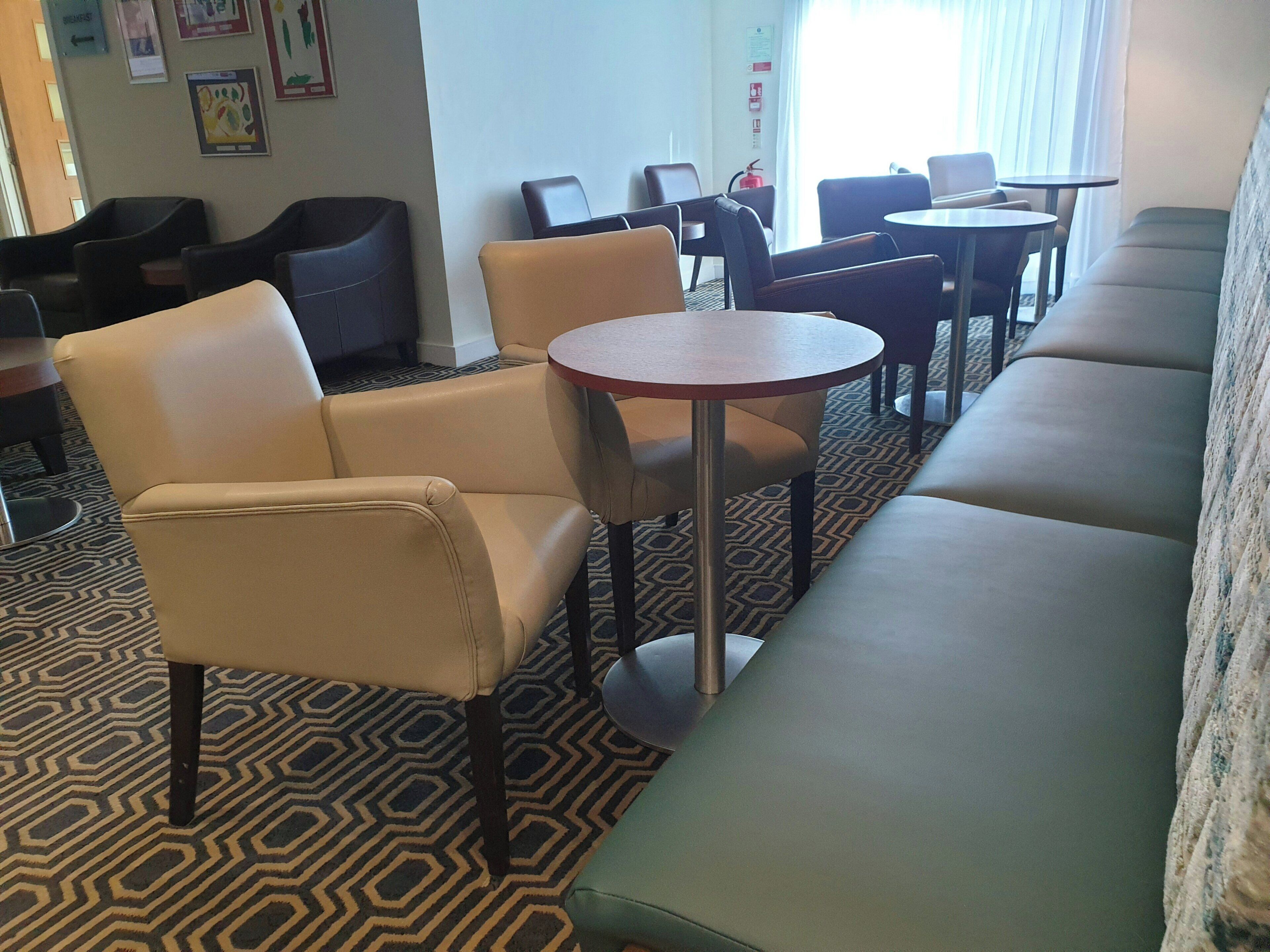 A hotel lobby with a patterned carpet, leather seating, and a fire extinguisher on the wall.