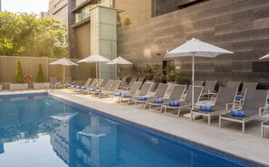 A poolside area with lounge chairs and umbrellas, a clear pool, and a building with a modern design.