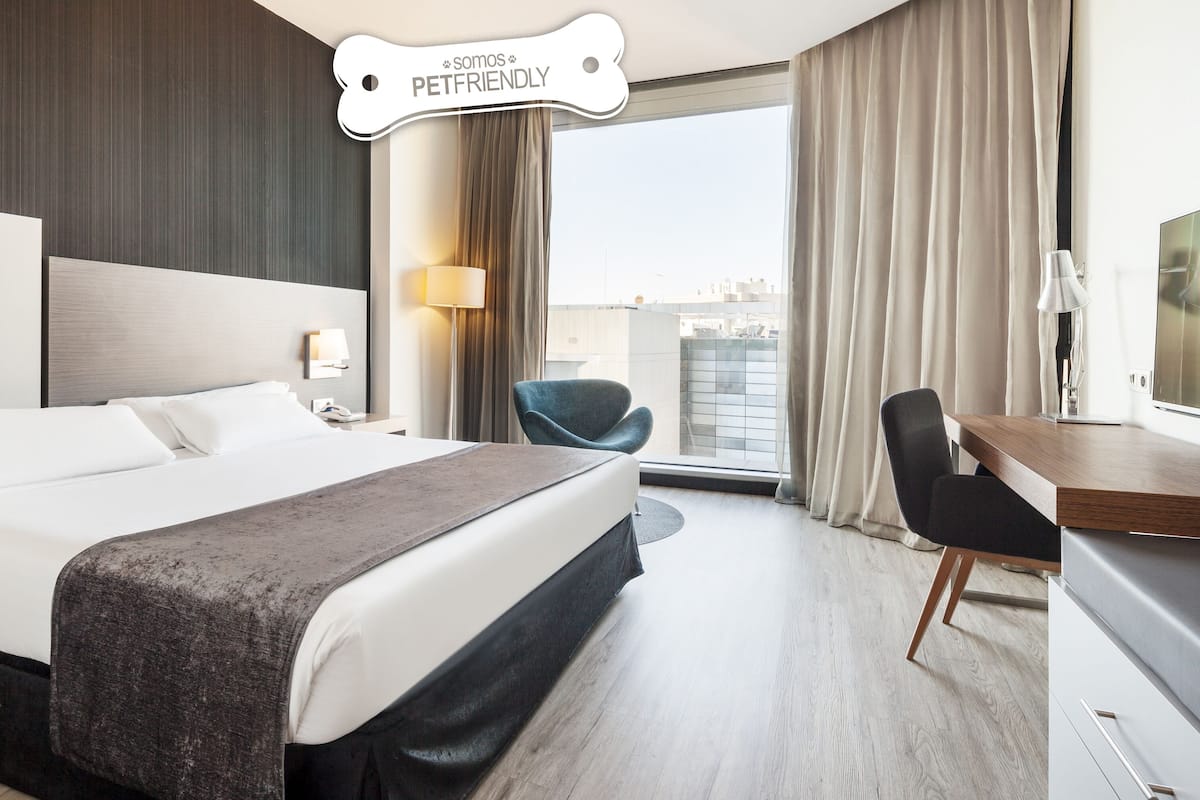 Una moderna camera d'albergo con un letto grande, una scrivania, una sedia e vista sulla città.